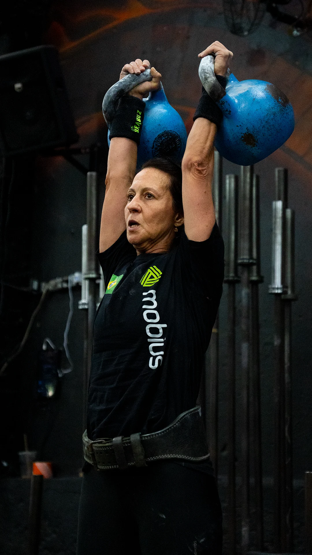 Atleta elevando dois kettlebells azuis acima da cabeça